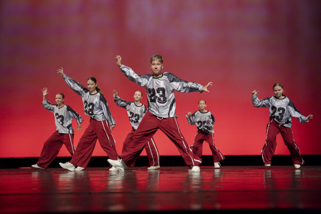 Detská hip hop skupina Tanečnej školy NEXUM počas vystúpenia v divadle, tanečníci v strieborných dresoch a bordových nohaviciach