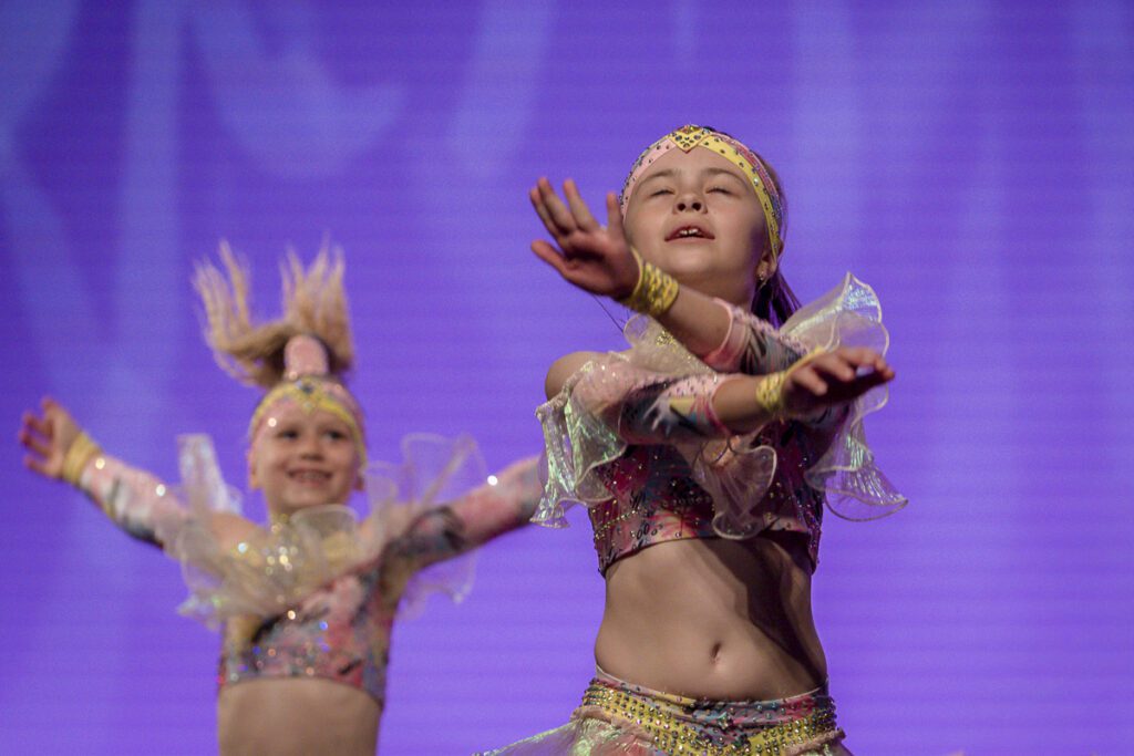 Dievčatá z krúžku mini kids disco dance Tanečnej školy NEXUM na vystúpení, v trblietavých kostýmoch na fialovom pozadí